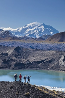A group of hikers stand on moraine next to a glacial meltpond at the edge of the Muldrow A group of hikers stand on moraine next to a glacial meltpond at the edge of the Muldrow