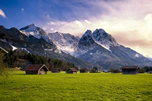 Huts in field at base of Bavarian Alps with snow at sunset Huts in field at base of Bavarian Alps with snow at sunset