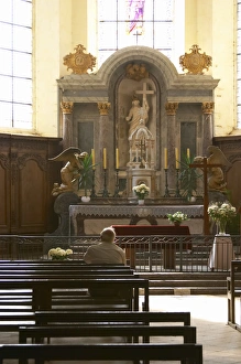 A man contemplating on a bench in a church in front of the altar with a ray of sunshine A man contemplating on a bench in a church in front of the altar with a ray of sunshine