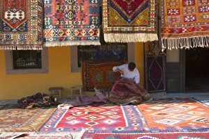 Man sewing the sides of a kilim in front of a local carpets shop, Pergamon (Pergamum Man sewing the sides of a kilim in front of a local carpets shop, Pergamon (Pergamum