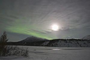 The moon rises over a curtain of green aurora borealis shimmering over the Middle The moon rises over a curtain of green aurora borealis shimmering over the Middle