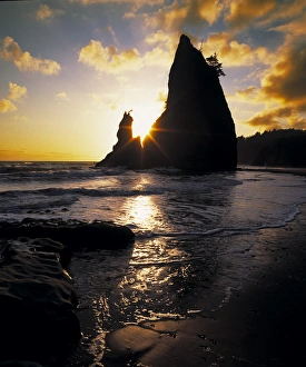 A seastack juts skyward with the setting suns rays streaking through a cleft in the rock A seastack juts skyward with the setting suns rays streaking through a cleft in the rock