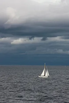 A small sailboat makes its way through the waters of Puget Sound under dark storm clouds A small sailboat makes its way through the waters of Puget Sound under dark storm clouds