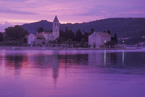 The sun sets behind the Franciscan Monastery on Prirovo Peninsula. Vis Harbor, Vis Island The sun sets behind the Franciscan Monastery on Prirovo Peninsula. Vis Harbor, Vis Island