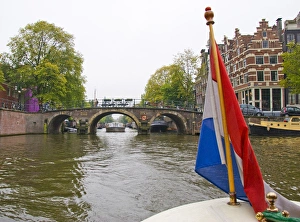 View from the front of a boat with a colorful flag, traveling a canal towards a bridge View from the front of a boat with a colorful flag, traveling a canal towards a bridge