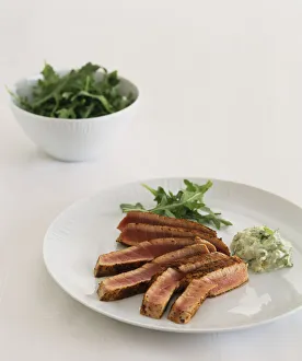 Cinnamon seared fresh tuna steak with bowl of rocket salad in background Cinnamon seared fresh tuna steak with bowl of rocket salad in background