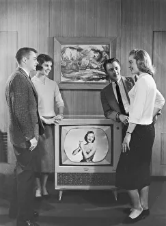 Two couples standing next to television Two couples standing next to television