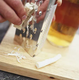 Grating horseradish root onto wooden chopping board, close-up Grating horseradish root onto wooden chopping board, close-up