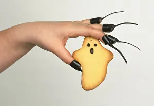 Hand wearing black plastic nails holding a Halloween ghost biscuit Hand wearing black plastic nails holding a Halloween ghost biscuit