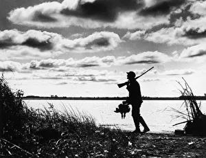 Silhouette of duck hunter walking along lake Silhouette of duck hunter walking along lake