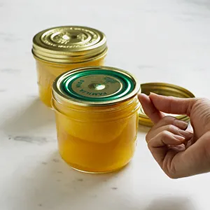 Using fingernail to test lid vacuum on a jar of preserved peaches, close-up Using fingernail to test lid vacuum on a jar of preserved peaches, close-up