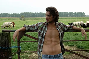Bare-chested cowboy leaning on a cow gate Bare-chested cowboy leaning on a cow gate