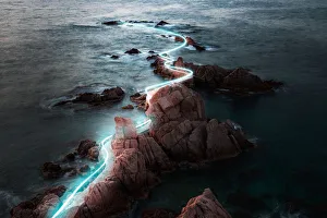 Blue light trail following footpath between the stunning coastline during sunrise Blue light trail following footpath between the stunning coastline during sunrise