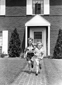 Boy and girl running on sidewalk in front of house Boy and girl running on sidewalk in front of house