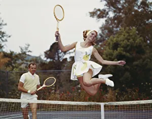Couple on tennis court, woman jumping in foreground Couple on tennis court, woman jumping in foreground