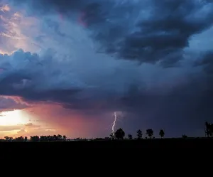 A dramatic thunderstorm at sunset with a forked lightning strike against a dramatically A dramatic thunderstorm at sunset with a forked lightning strike against a dramatically