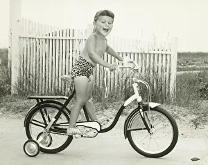 Girl (6-7) riding bicycle with side wheels, (B&W) Girl (6-7) riding bicycle with side wheels, (B&W)