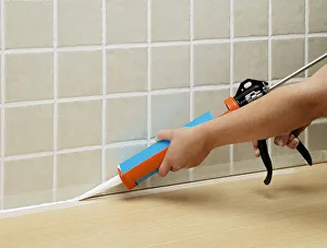 Hands applying sealant to tiles with sealant tube Hands applying sealant to tiles with sealant tube