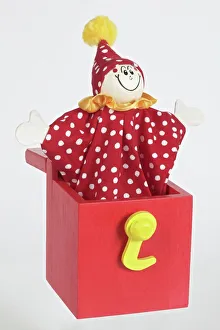 Jack in a box, smiling clown puppet popping out of red wooden box with arms extended to Jack in a box, smiling clown puppet popping out of red wooden box with arms extended to