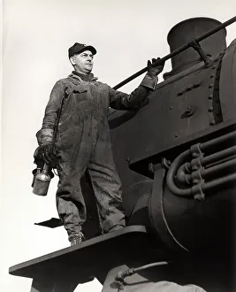 Man standing on train engine, holding oil can Man standing on train engine, holding oil can