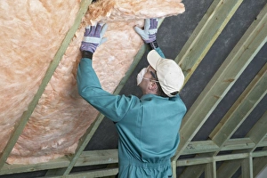 Man wearing overalls, mask, gloves and cap, filling the space between rafters with an Man wearing overalls, mask, gloves and cap, filling the space between rafters with an