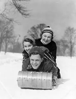 Man And Two Women Wearing Wool Hats And Winter Clothing Tobogganing In Snow With Tree Man And Two Women Wearing Wool Hats And Winter Clothing Tobogganing In Snow With Tree