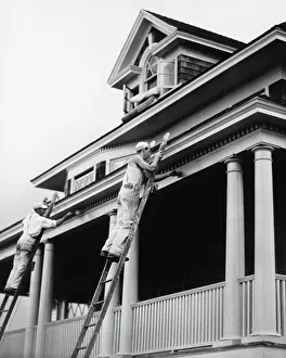 Two manual workers on ladders painting house exterior, (B&W) Two manual workers on ladders painting house exterior, (B&W)