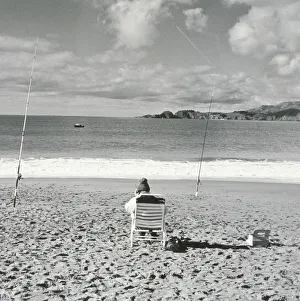 Person sitting on beach with fishing poles embedded in sand and using cell phone Person sitting on beach with fishing poles embedded in sand and using cell phone