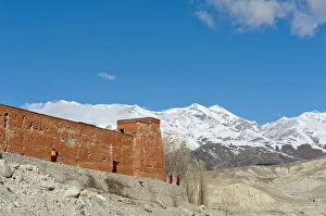 Red wall of a building with monks, Choede Gompa monastery, snow-capped mountains of Mustang Himal mountain range at Red wall of a building with monks, Choede Gompa monastery, snow-capped mountains of Mustang Himal mountain range at