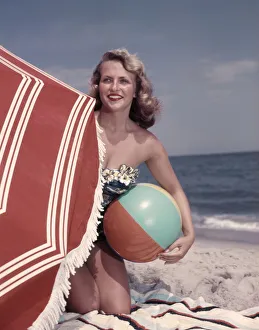 Smiling Blonde Woman Bathing Suit Hold Beach Ball Kneel In Sand By Red Sun Umbrella Smiling Blonde Woman Bathing Suit Hold Beach Ball Kneel In Sand By Red Sun Umbrella