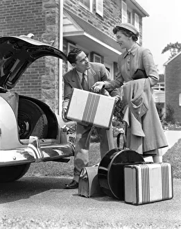 Smiling couple load suitcases into trunk of sedan Smiling couple load suitcases into trunk of sedan