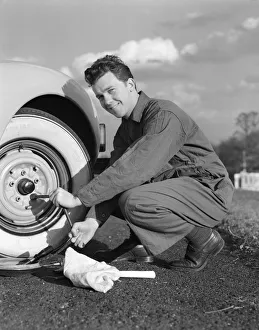 Smiling man in coveralls using tire iron to change tire on sedan Smiling man in coveralls using tire iron to change tire on sedan