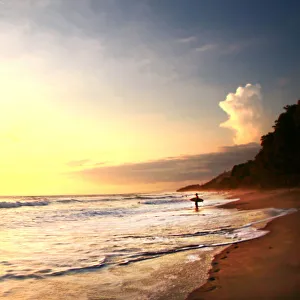 Surfer stands in ocean watching sunset on beach Surfer stands in ocean watching sunset on beach