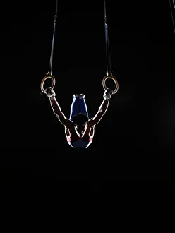 Teenage (16-17) male gymnast practicing on rings against black background Teenage (16-17) male gymnast practicing on rings against black background