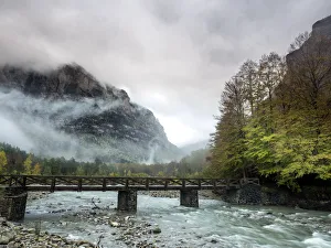 Torrent of high mountain with a bridge of wood in a valley with mountains and forests in autumn Torrent of high mountain with a bridge of wood in a valley with mountains and forests in autumn
