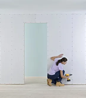 Woman holding screwdriver to wall of plasterboard Woman holding screwdriver to wall of plasterboard
