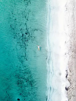 Woman takes a bath and floats in a turquoise sea. Stintino, Sardinia, Italy. Aerial view Woman takes a bath and floats in a turquoise sea. Stintino, Sardinia, Italy. Aerial view
