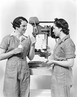 Two women workers standing near drill press, eating sandwich and drinking milk Two women workers standing near drill press, eating sandwich and drinking milk