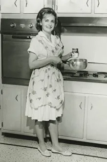 Young woman holding can of soup and pot in kitchen, (B&W) Young woman holding can of soup and pot in kitchen, (B&W)