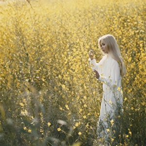 Young woman standing in field holding flower Young woman standing in field holding flower