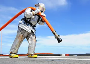 Firefighter carries a charged hose across the flight deck of USS Denver Firefighter carries a charged hose across the flight deck of USS Denver