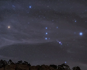 The Orion constellation rises over a hill through high thin clouds The Orion constellation rises over a hill through high thin clouds