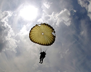 A paratrooper descends through the sky during the day A paratrooper descends through the sky during the day