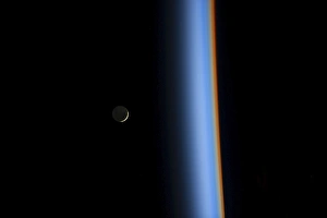 View of a crescent moon rising and the cusp of Earths atmosphere View of a crescent moon rising and the cusp of Earths atmosphere