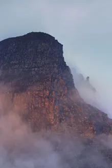 The rugged cliffs of Stac Pollidh in cloud and mist and lit by evening light The rugged cliffs of Stac Pollidh in cloud and mist and lit by evening light