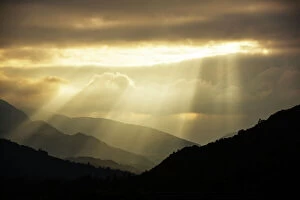 Ambleside Collection: Shafts of light at dusk over Wrynose pass and the Coniston hills from Ambleside, Lake District