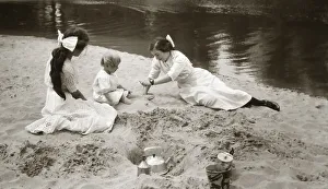 Two girls with a baby playing on the beach at the water's edge with bucket, spade Two girls with a baby playing on the beach at the water's edge with bucket, spade