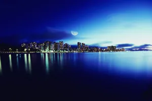 Hawaii, Oahu, Honolulu, Waikiki skyline at night, moon overhead, view from ocean Hawaii, Oahu, Honolulu, Waikiki skyline at night, moon overhead, view from ocean
