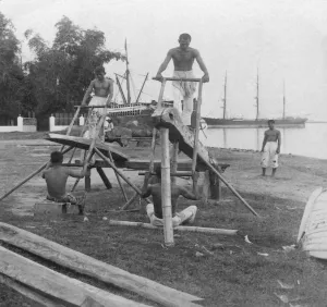 Historic image in black and white of men working a manual mill cutting wooden logs on an island in the Philippines Historic image in black and white of men working a manual mill cutting wooden logs on an island in the Philippines