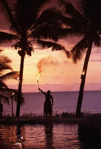 Native In A Grass Skirt Holding A Flaming Torch By Coast At Sunset Native In A Grass Skirt Holding A Flaming Torch By Coast At Sunset